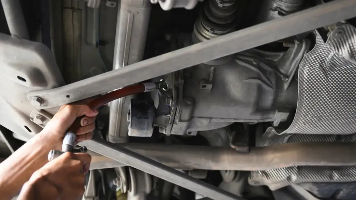 Wymiana oleju w tylnym moście. Mechanik używa wężyka do uzupełnienia płynu.