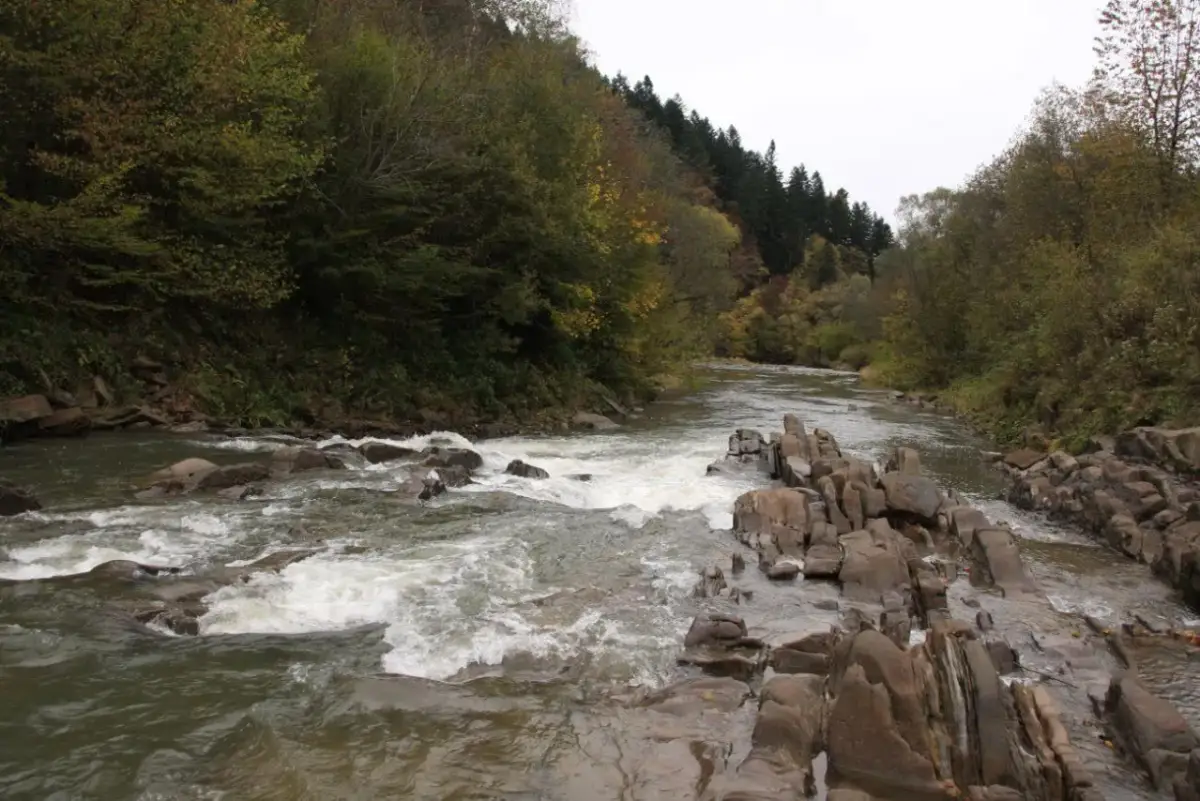 Wodospady i kamieniste koryto rzeki w rezerwacie przyrody Sine Wiry. Jesienne drzewa otaczają rwący nurt.