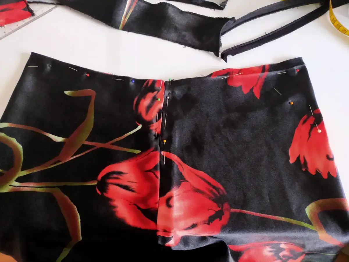 Szpilki spinają czarną tkaninę w czerwone kwiaty, przygotowując ją do przerobienia sukienki na kombinezon.