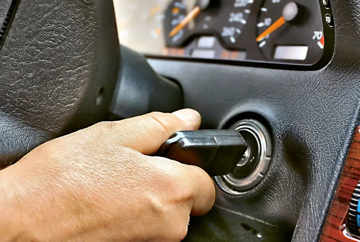 Dłoń przekręca kluczyk w stacyjce. Samochód odpala i gaśnie benzyna, co sugeruje problem z paliwem.