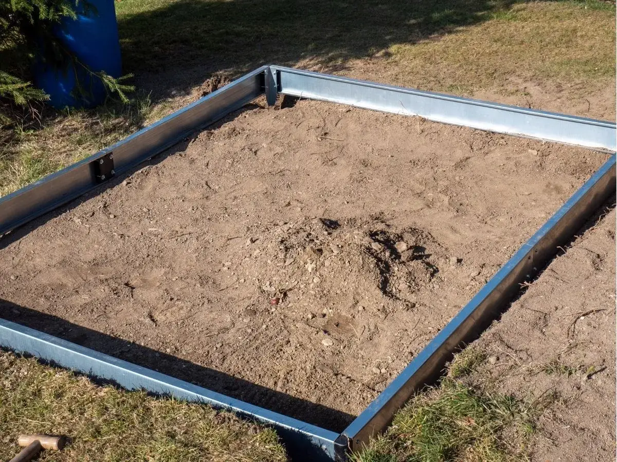 Metalowa rama wyznacza teren pod budowę szklarni. To pierwszy krok, jak zrobić fundament pod szklarnię, przygotowując podłoże.