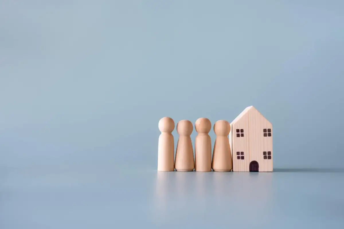 Drewniane figurki ludzi stoją obok domku. Symbolizują rodzinę i jej dom, pokazując, jak zachować mieszkanie przy upadłości.