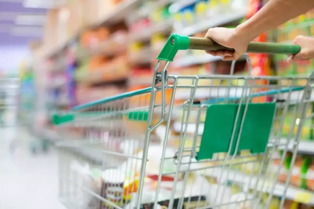 Ręka pcha wózek sklepowy w alejkach sklepu spożywczego, tworząc obraz dynamicznego doświadczenia w branży retail.