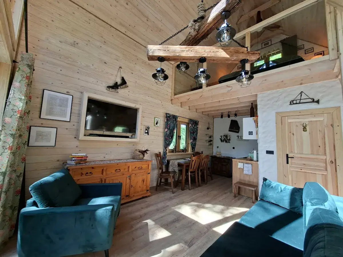 Przytulne wnętrze drewnianego domku z kanapą, telewizorem i aneksem kuchennym.