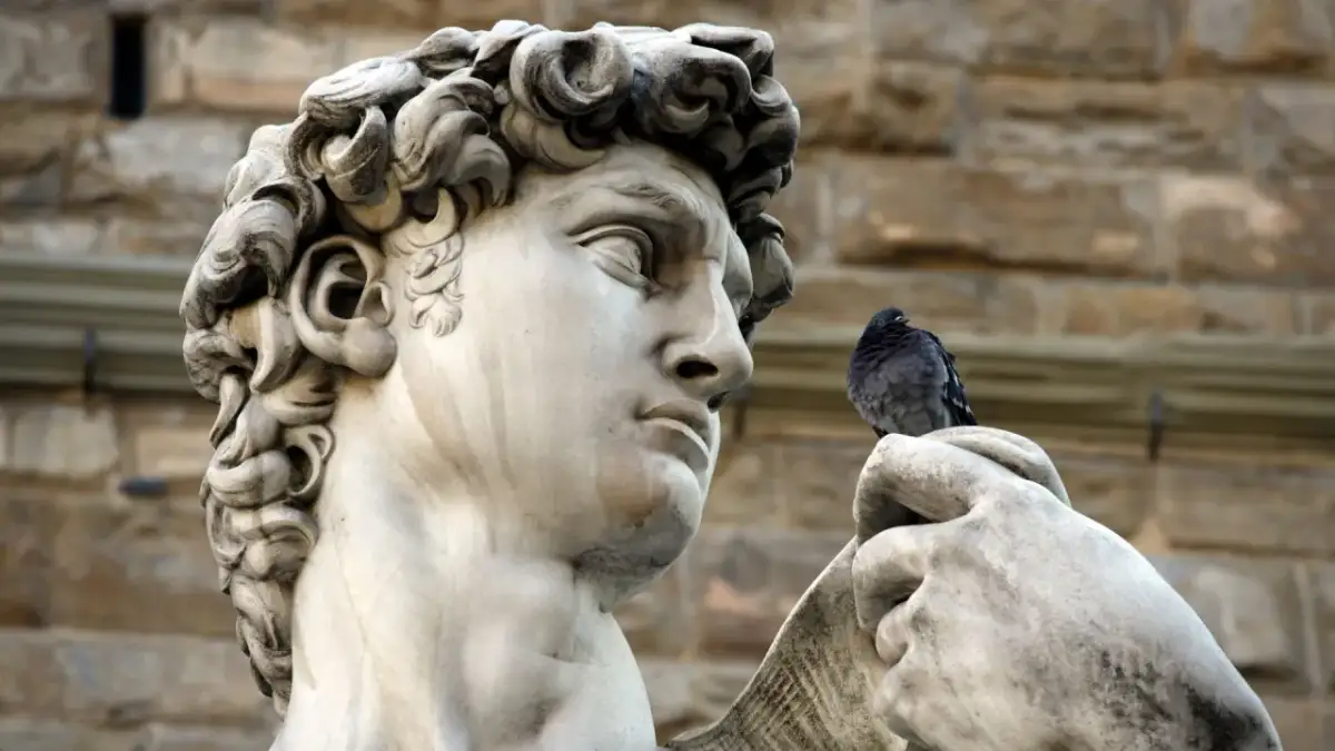 Michał Anioł rzeźba Dawida z gołębiem na dłoni. Marmurowa postać z kamiennym spojrzeniem.