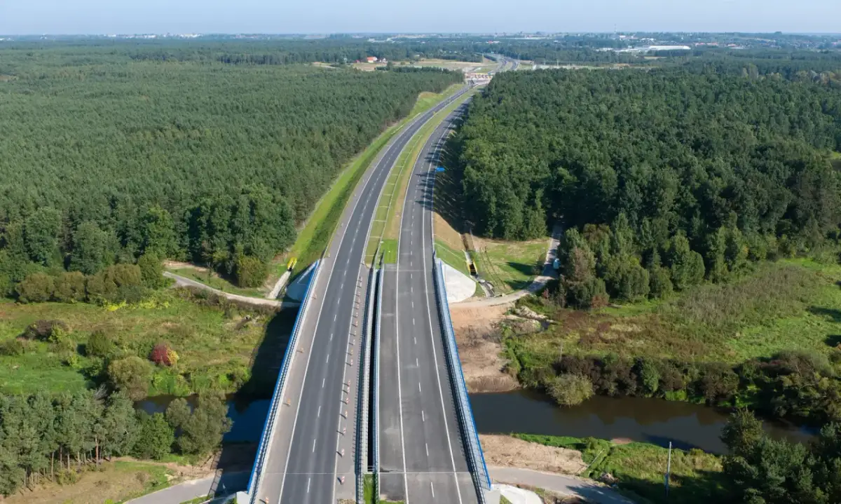 Widok z lotu ptaka na autostradę A1 otoczoną lasem, z mostem nad rzeką.