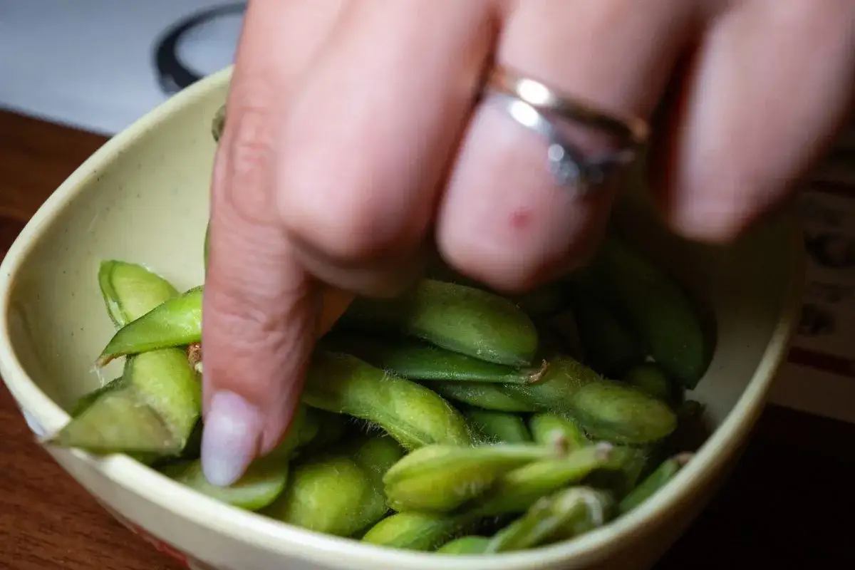 Ręka sięga po zielone strączki edamame w miseczce. Zdrowa przekąska, co zamiast Controloc?