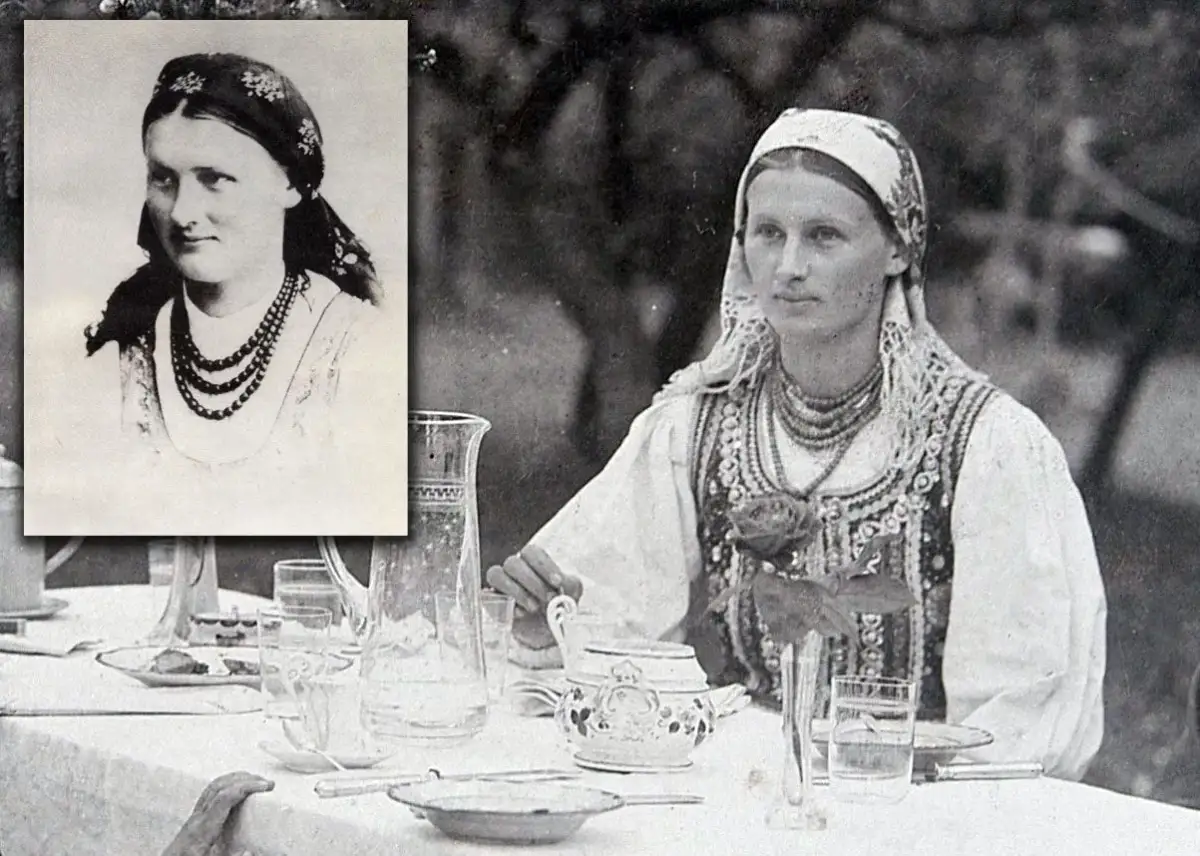 Chłopomania w weselu: młoda kobieta w tradycyjnym stroju, z naszyjnikami i chustą na głowie, siedzi przy stole nakrytym do obiadu.