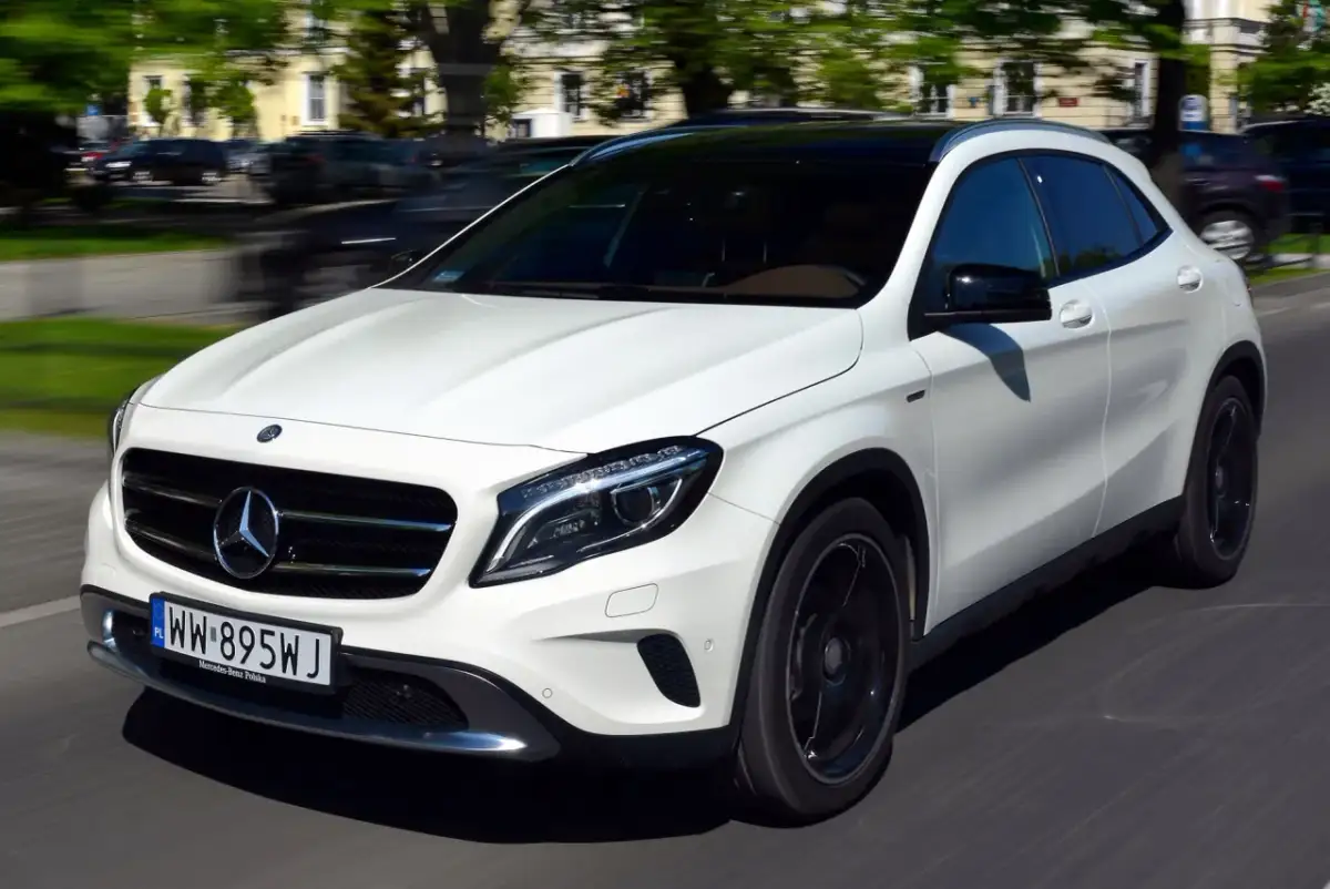 Biały Mercedes-Benz GLA AMG pędzi ulicą, jego sportowy wygląd podkreślają czarne felgi i przyciemniany dach.
