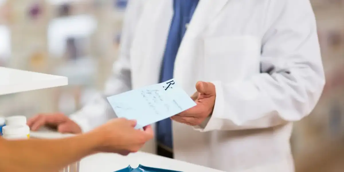 Farmaceuta w białym fartuchu podaje receptę. Dowiedz się, jak odzyskać kod recepty, aby zrealizować leki.