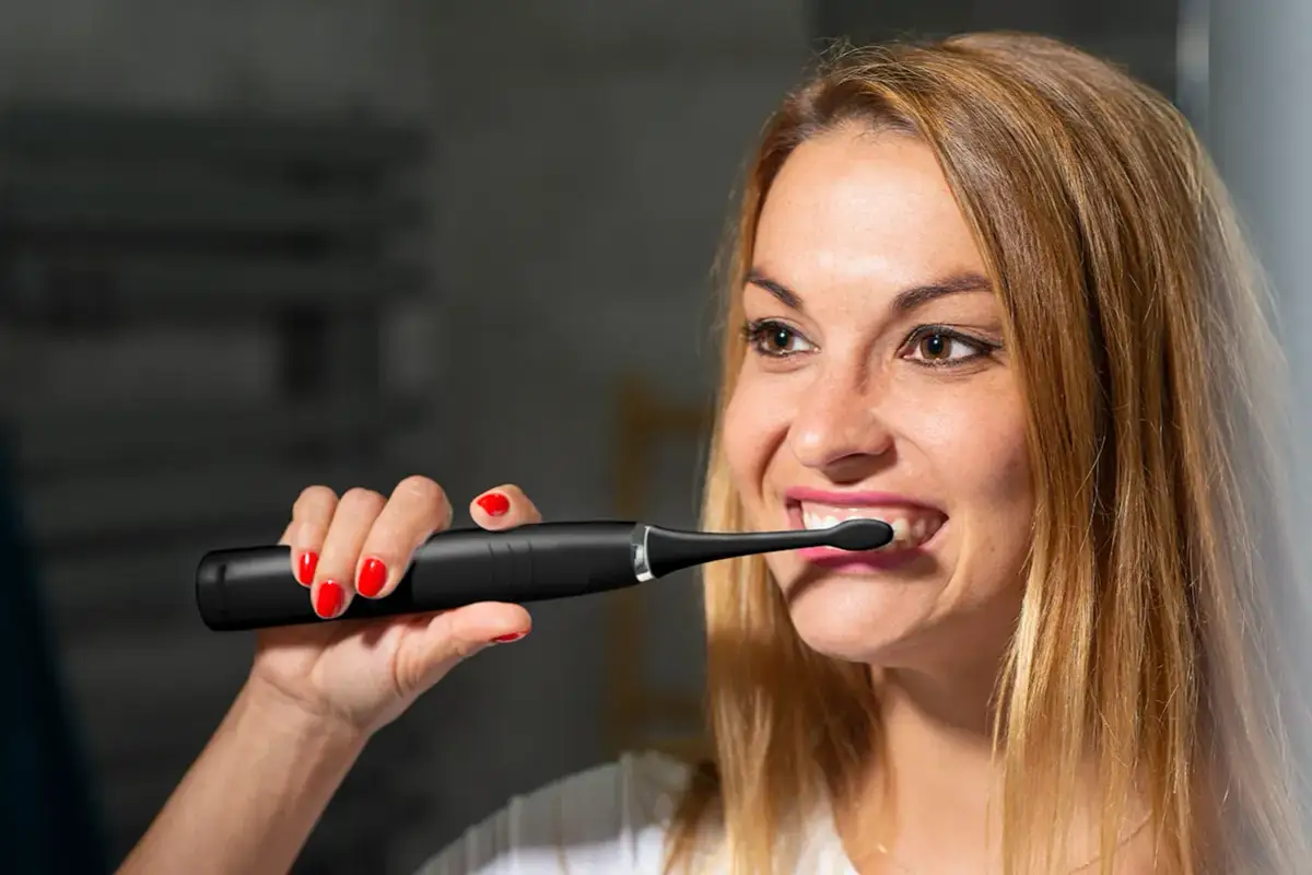 Kobieta z czerwonymi paznokciami używa czarnej szczoteczki sonicznej do zębów.
