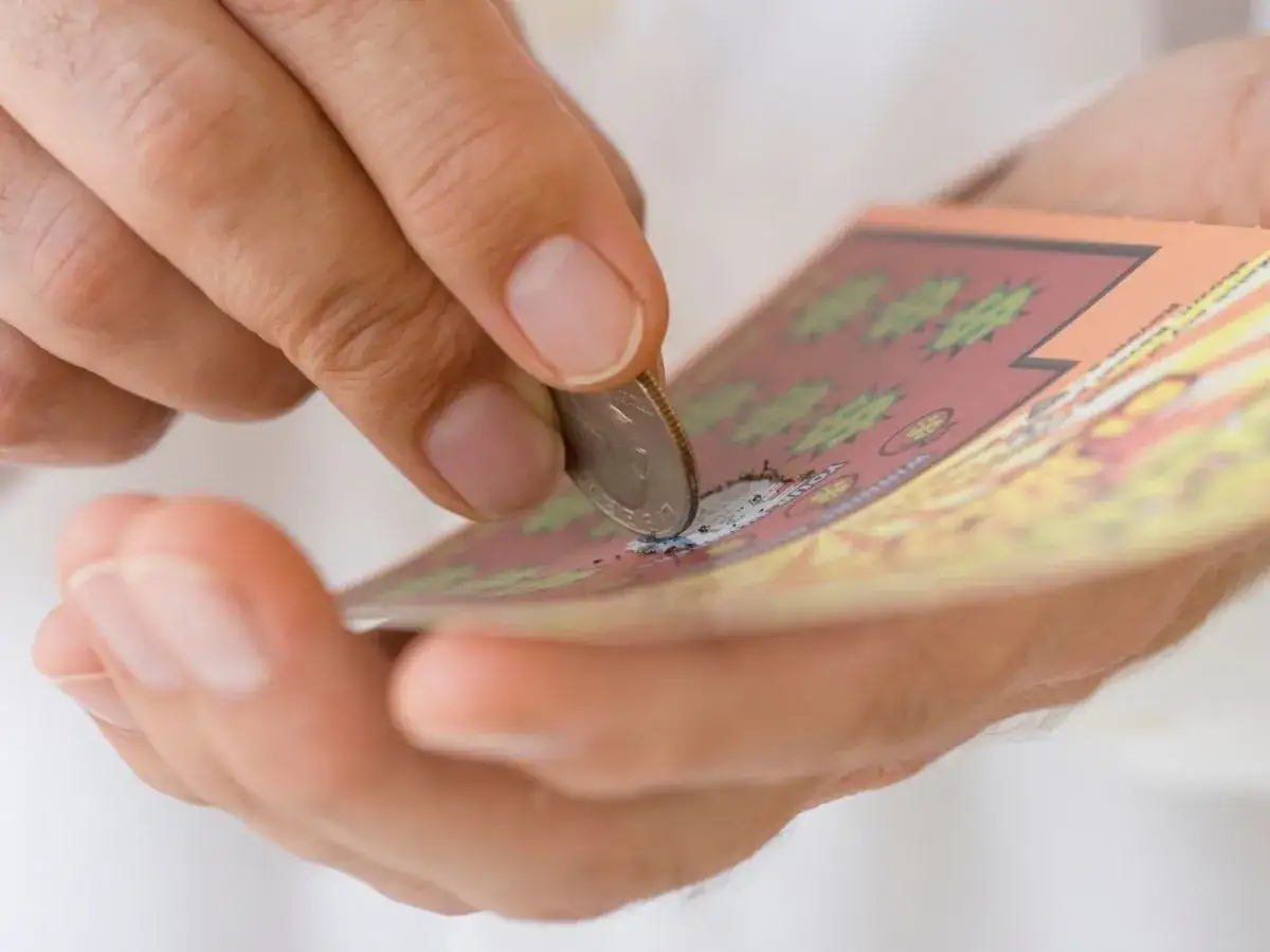 Dłoń zdrapuje monetą zdrapkę z symbolem dolara.