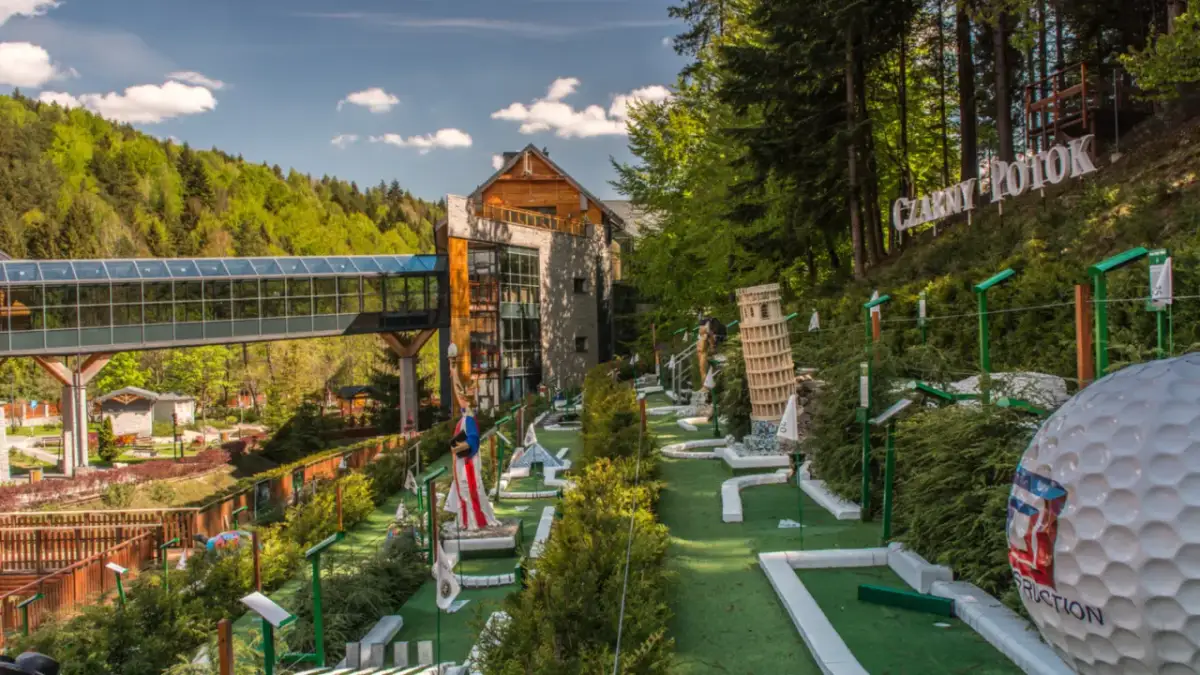 Mini golf z atrakcjami jak Krzywa Wieża w Pizie i Statua Wolności, obok budynku i lasu.
