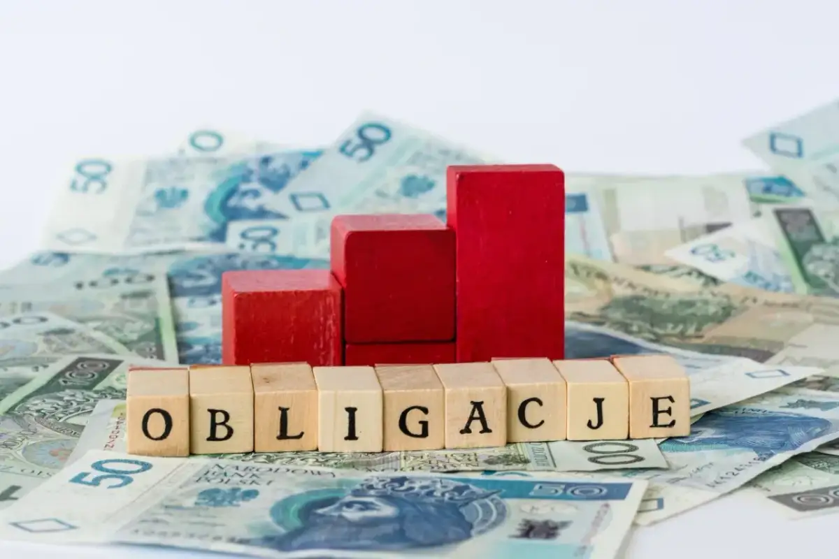 Drewniane klocki z napisem "OBLIGACJE" na tle polskich banknotów. Czy można kupić obligacje bez konta w PKO?