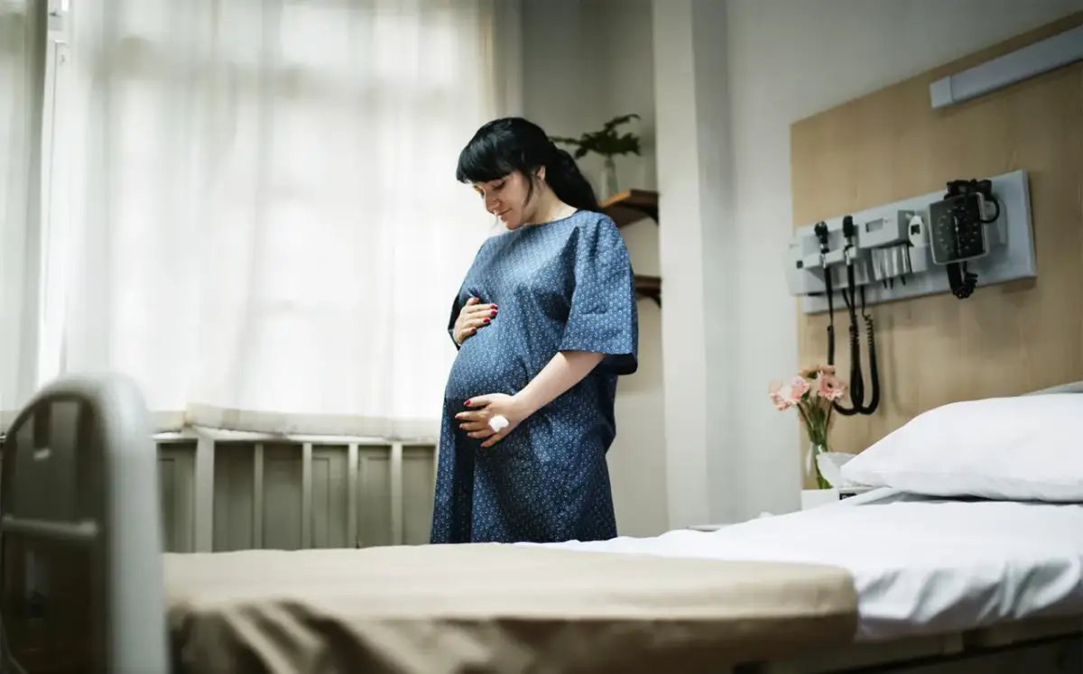 Kobieta w szpitalnej sali, trzymająca się za brzuch, szuka sposobów, jak złagodzić skurcze porodowe.