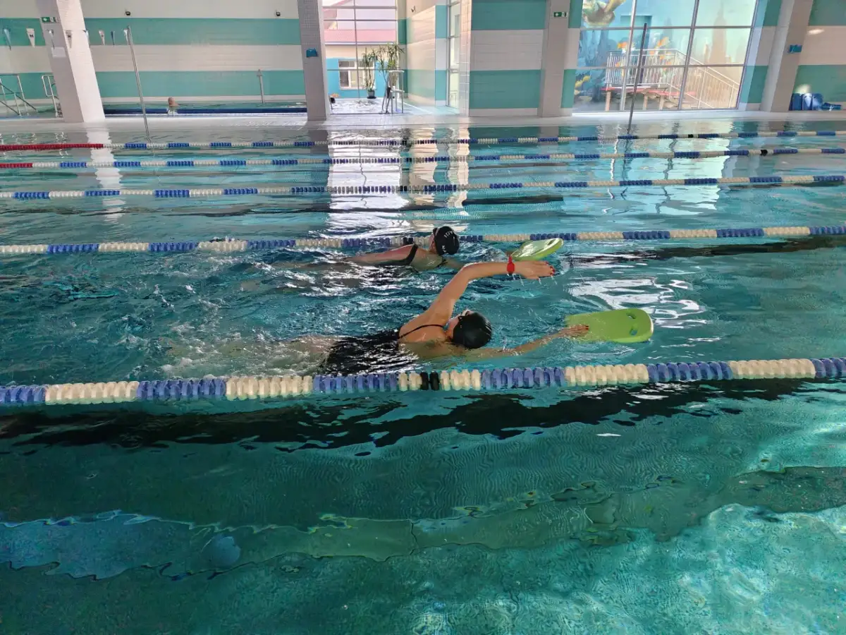 Dwie kobiety uczą się pływać, pokonując lęk przed wodą. Jedna z nich używa deski do pływania.