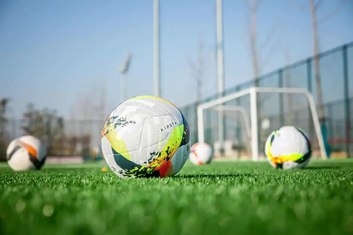 Piłki do piłki nożnej na zielonej murawie, z bramką w tle.