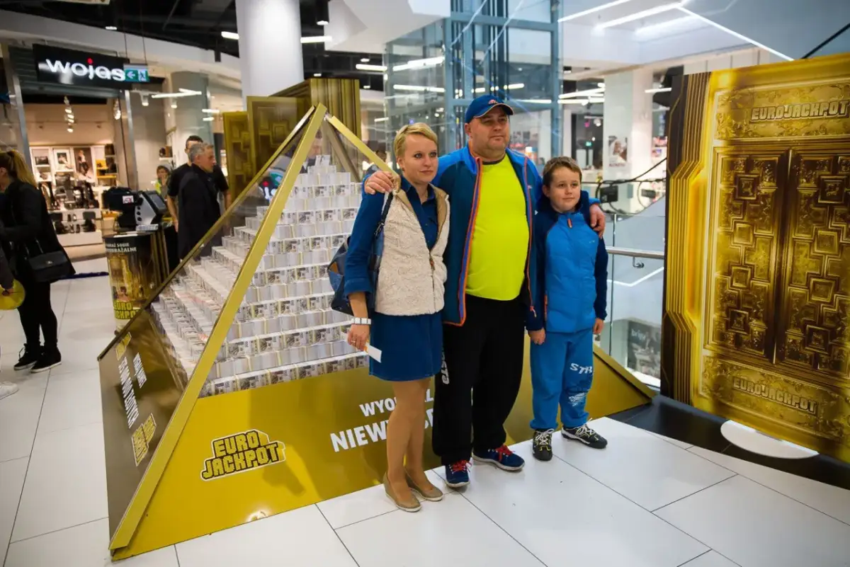 Rodzina pozuje przy piramidzie z pieniędzy, symbolizującej wygraną w Eurojackpot. Dowiedz się, eurojackpot jak odebrać wygraną.