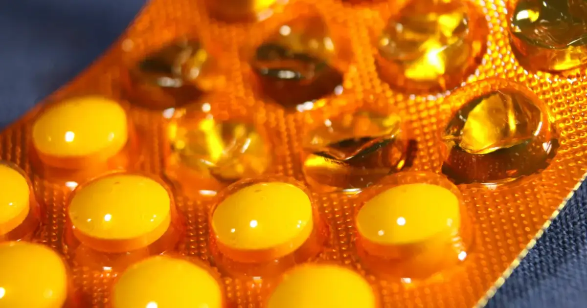 Zbliżenie na pomarańczową folię z żółtymi kapsułkami i tabletkami.