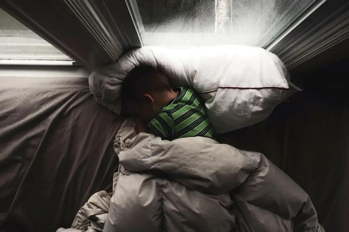 Chłopiec śpi pod kołdrą, przytulony do poduszki. Czy to początek lunatykowania?