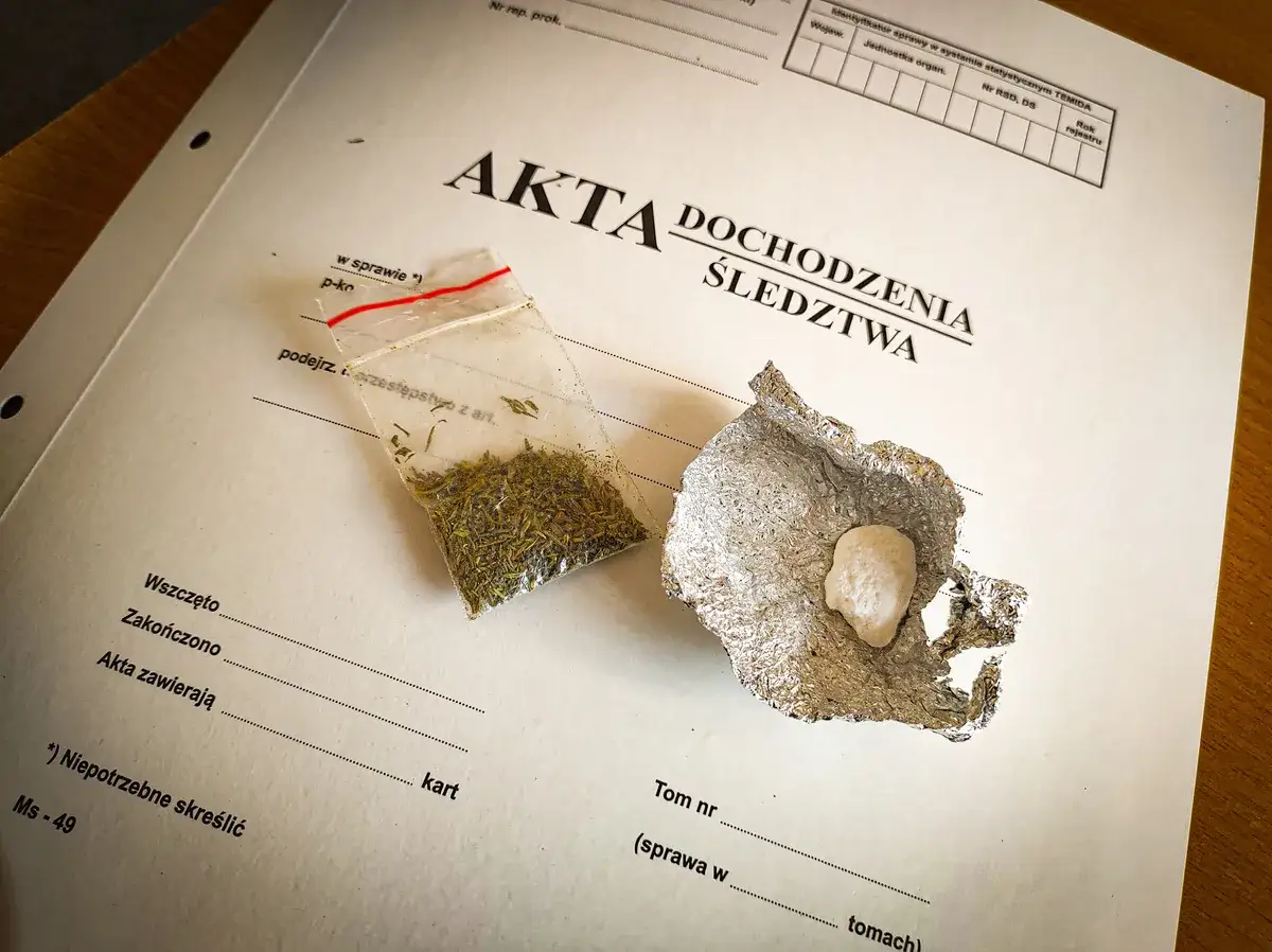 Mała torebka z suszem i grudka substancji w folii aluminiowej na dokumentach śledczych.