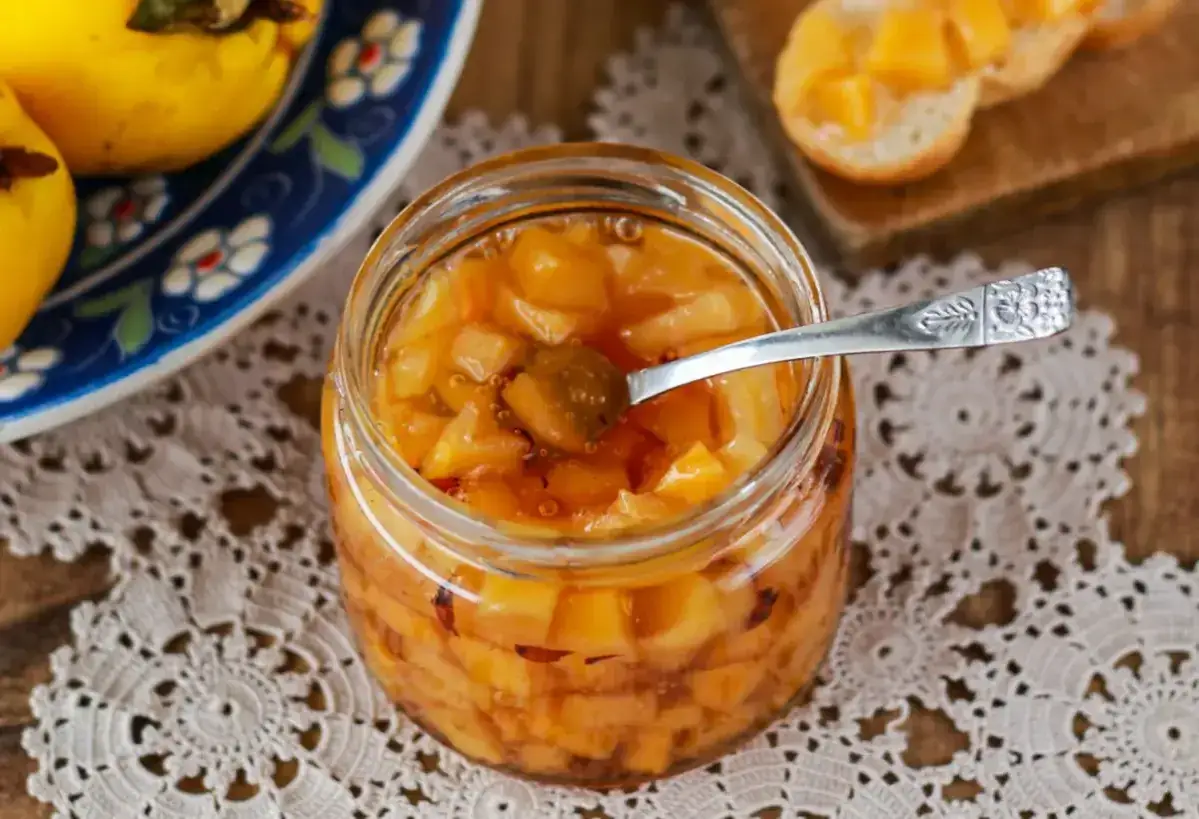 Słoik domowej konfitury z pigwy z łyżeczką, obok talerz z owocami.