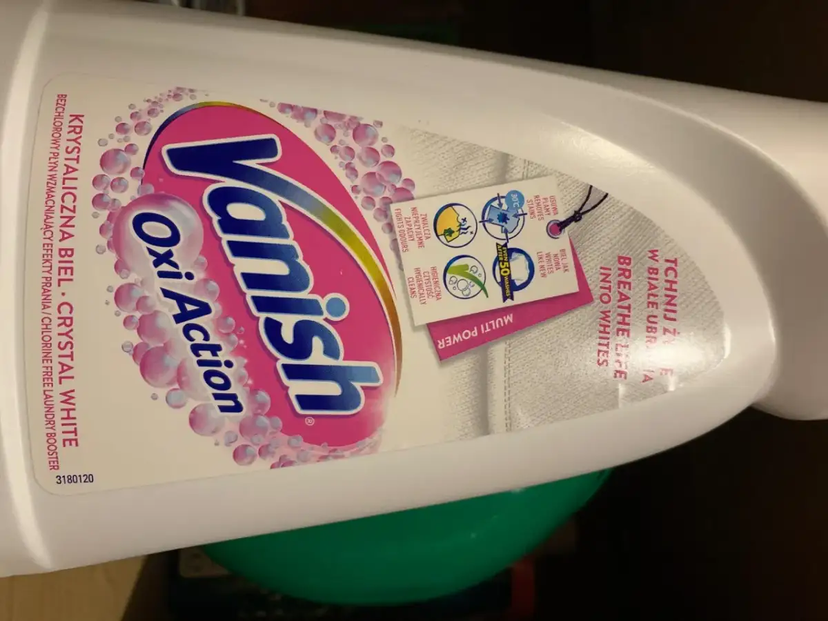Butelka płynu Vanish Oxi Action Crystal White z etykietą i zawieszką informującą o działaniu.