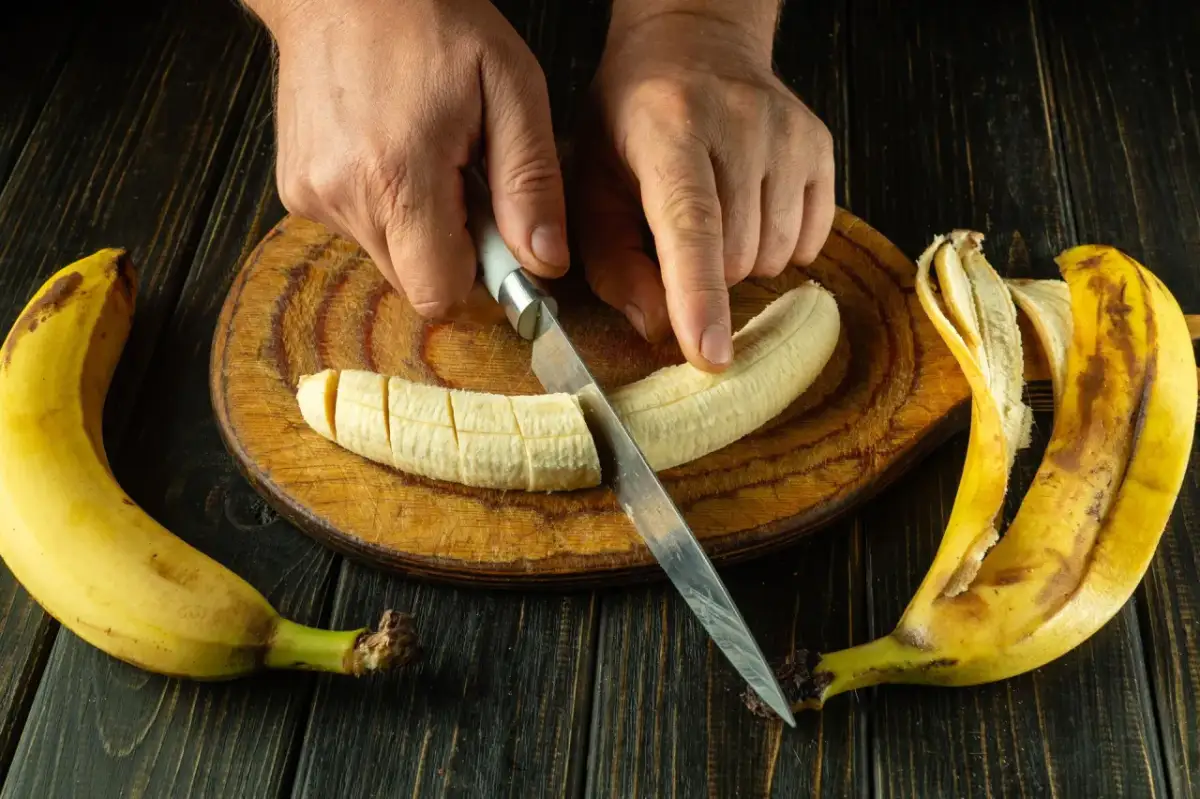 Dłonie kroją banana na desce. To świetny pomysł, co jeść na skurcze nóg, bo banany są bogate w potas.