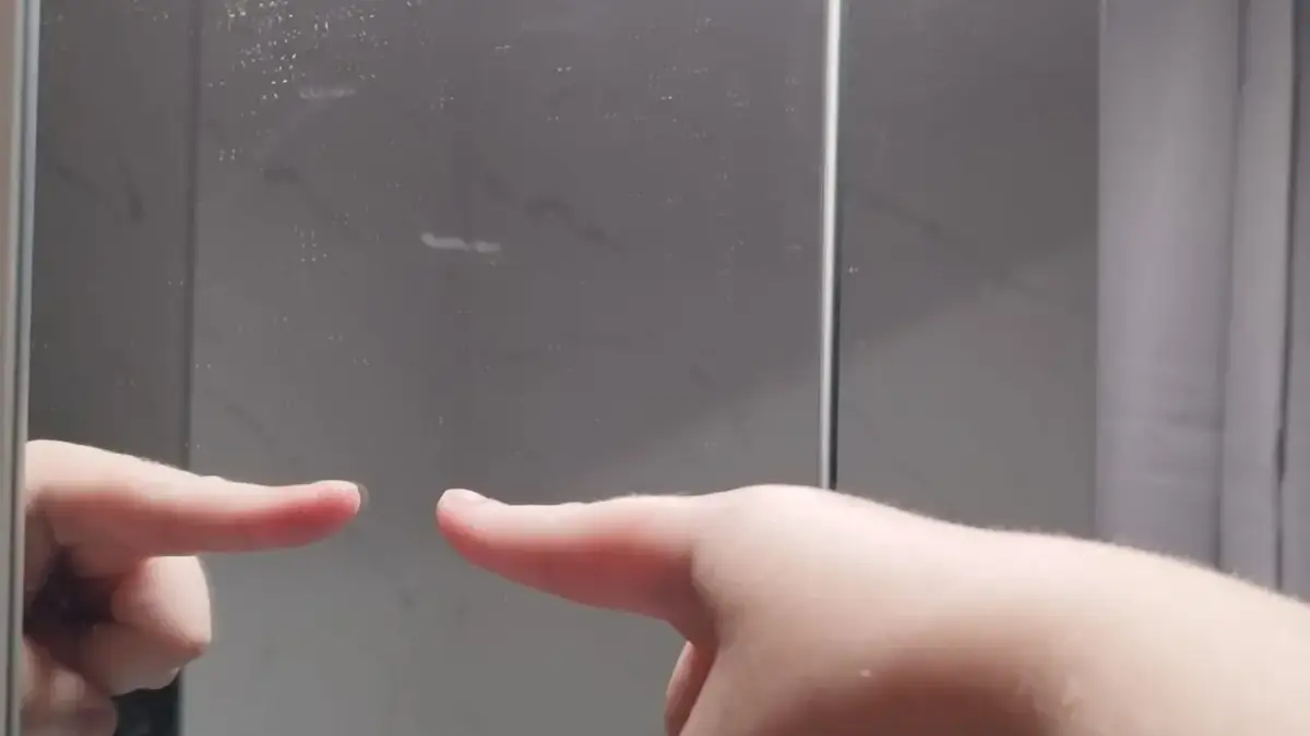 Palec wskazujący dotyka lustra, sprawdzając, jak sprawdzić czy lustro jest weneckie. Po drugiej stronie widać odbicie.