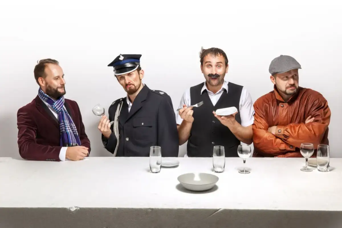 Czterech panów przy stole, jeden w garniturze, drugi w mundurze, trzeci z wąsami i sztućcami, czwarty w skórzanej kurtce. Scena jak z kabaretu z Kielc.