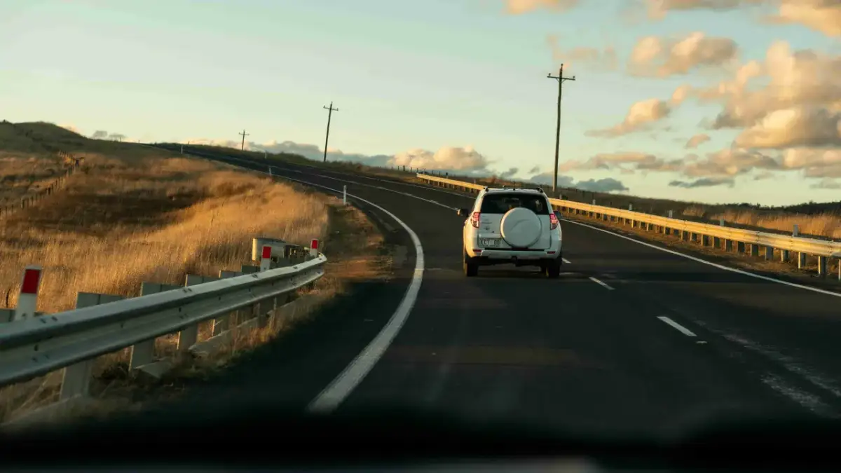 Biały SUV jedzie pustą drogą w Australii, otoczoną złotymi trawami i słupami telegraficznymi. Ruch drogowy jest minimalny.