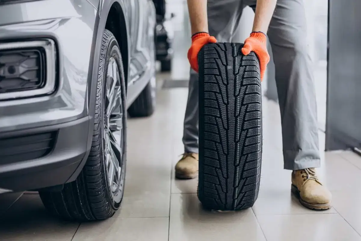 Mechanik w pomarańczowych rękawiczkach trzyma nowe opony letnie obok samochodu. Czas na test opon letnich!