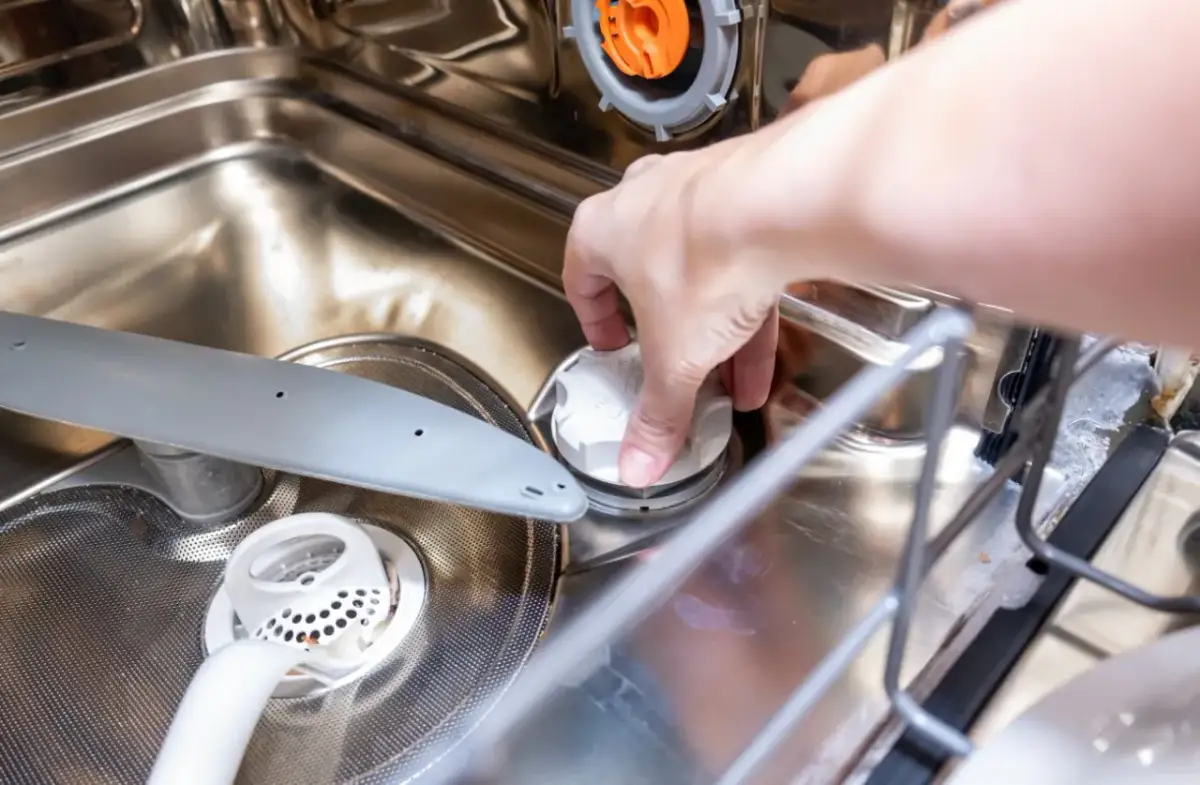 Dłoń zakręca białą nakrętkę, pokazując, gdzie wsypać sól do zmywarki.