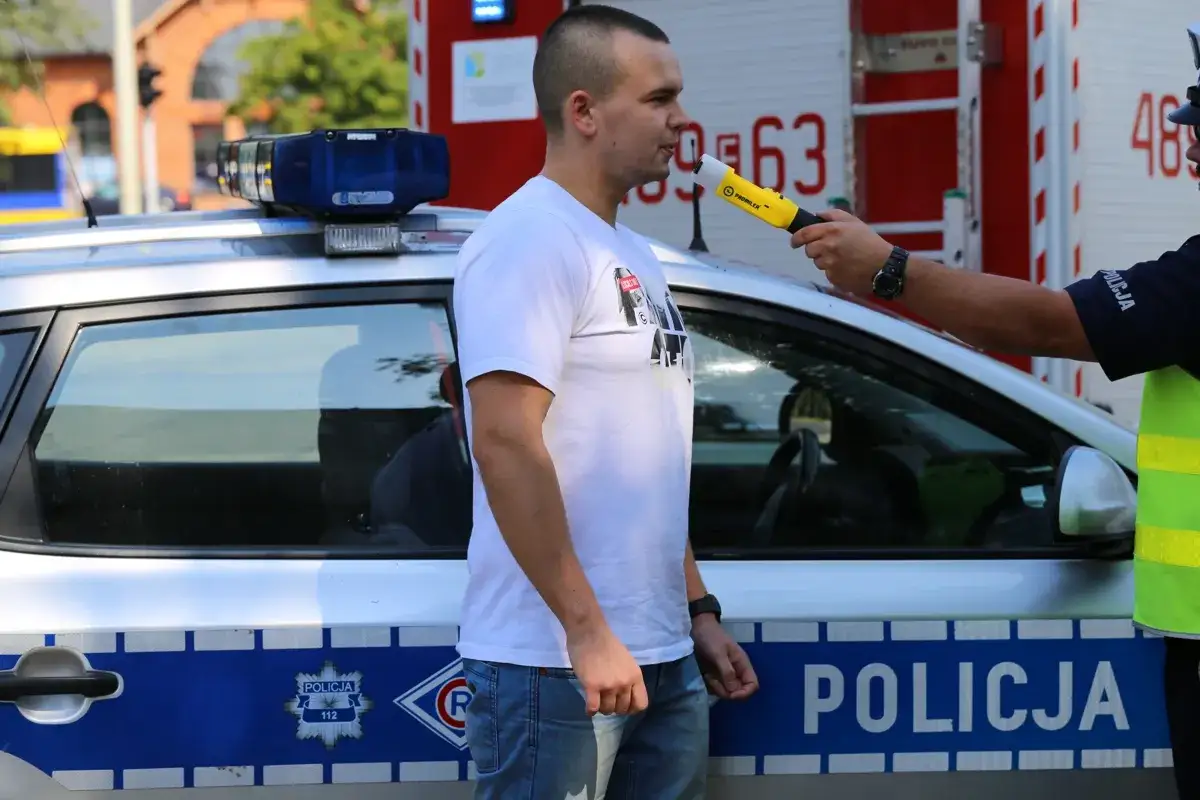Policjant bada alkomatem mężczyznę obok radiowozu.