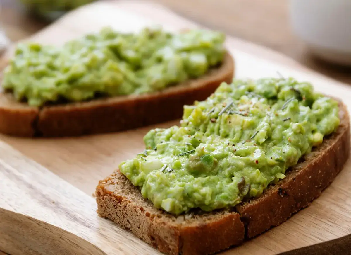 Pyszna pasta z awokado i serka na ciemnym pieczywie, posypana ziołami. Idealna na szybkie śniadanie.