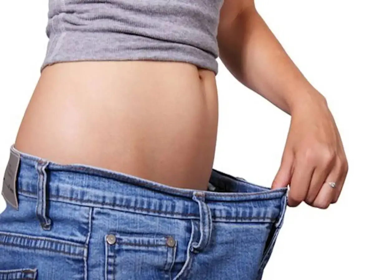 Kobieta w dżinsach pokazuje swój płaski brzuch.