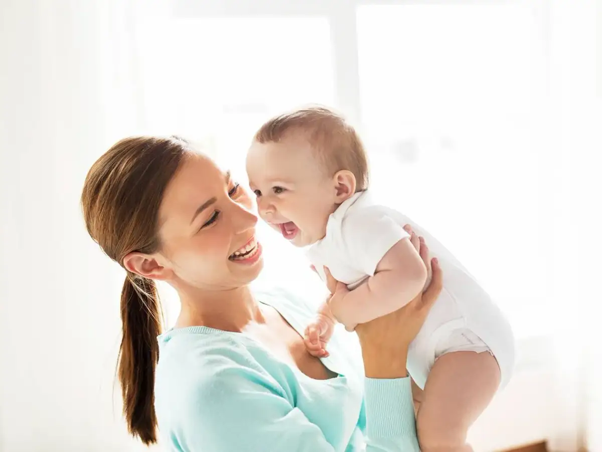 Szczęśliwa mama trzyma roześmiane dziecko. Zastanawiasz się, ile pieluch dziennie dla noworodka?