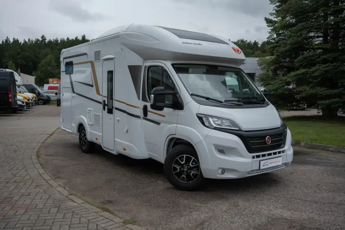 Biały van camper z brązowymi i czarnymi akcentami, zaparkowany na zewnątrz. Idealny do podróży i odkrywania nowych miejsc.