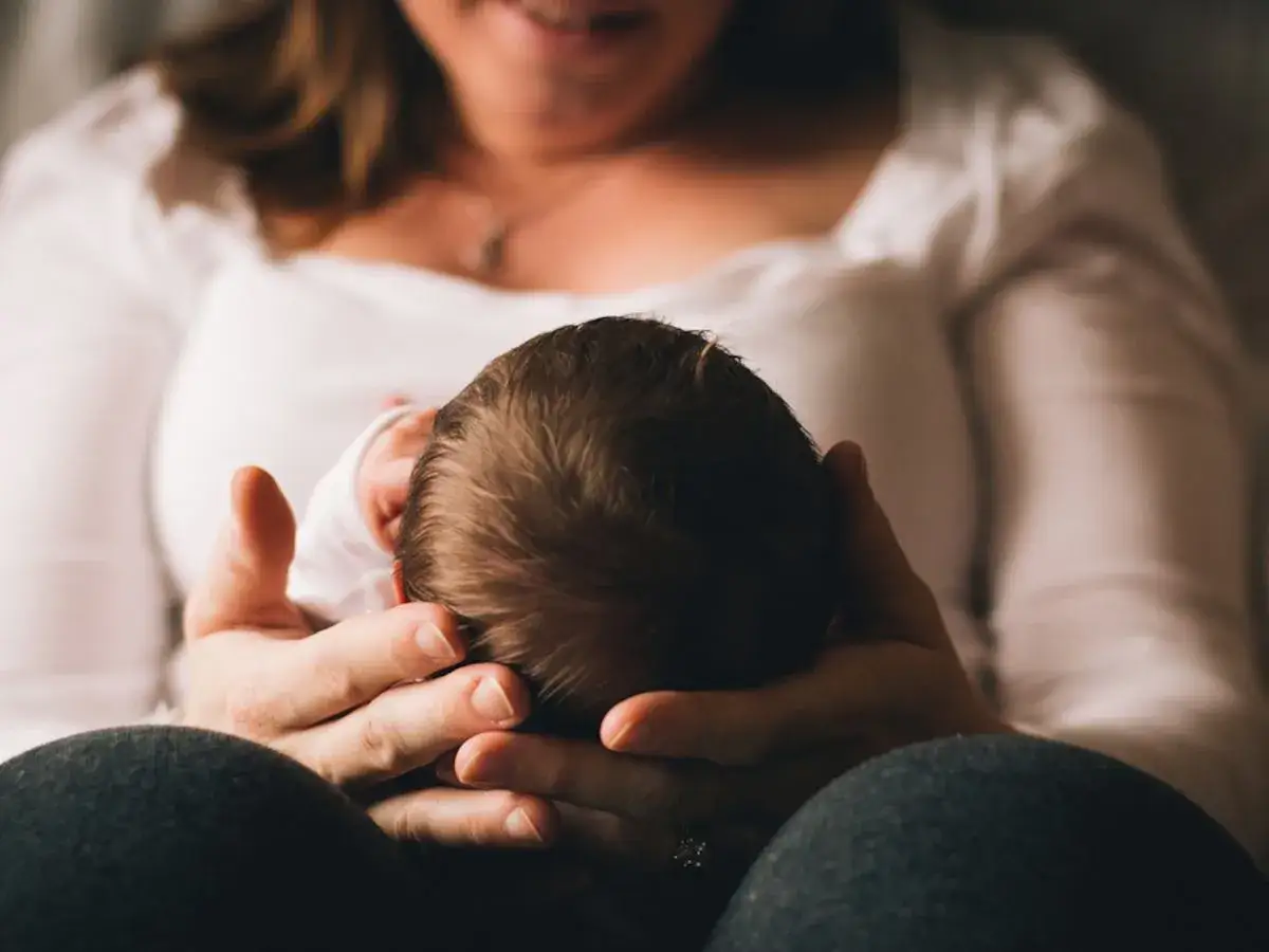 Dłoń matki trzymająca główkę noworodka.