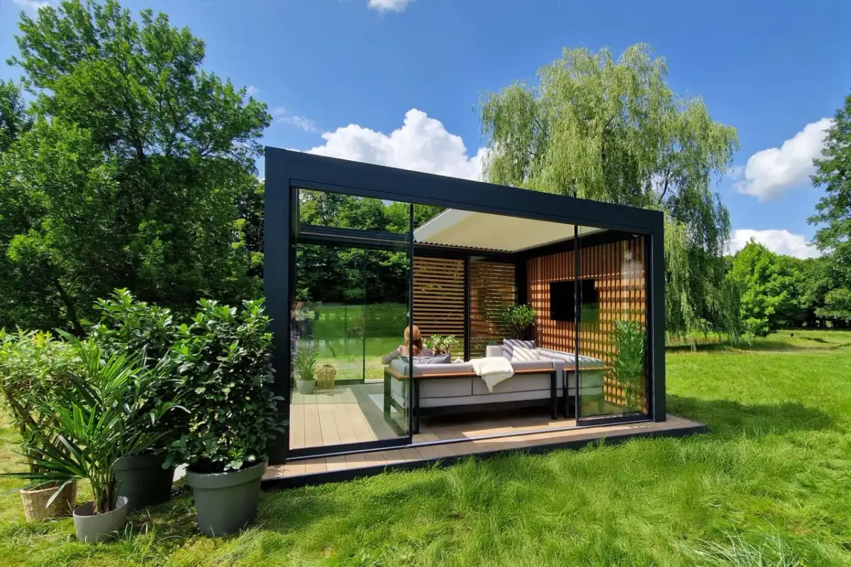 Nowoczesny pawilon ogrodowy z przeszklonymi ścianami i wygodną sofą, idealny na relaks. Pokazuje, jak zrobić taras na trawie, tworząc przytulną przestrzeń.