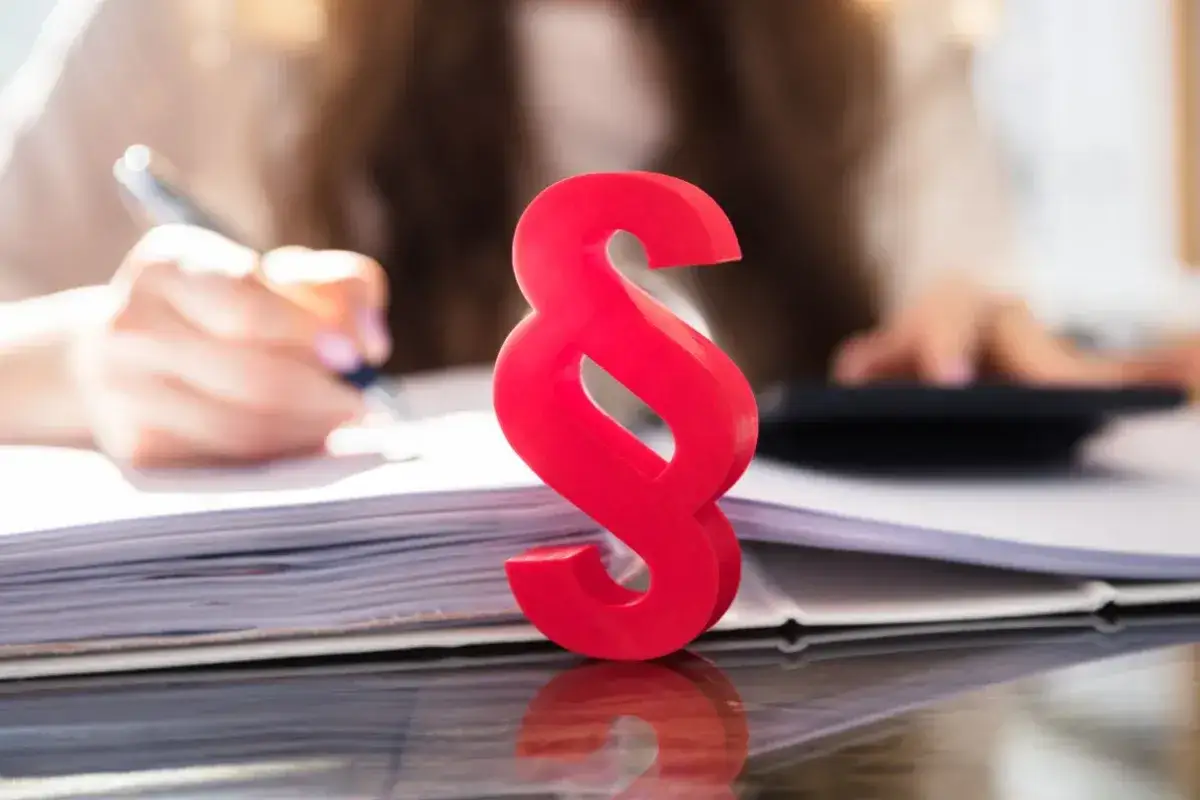 Czerwony paragraf symbolizuje prawne aspekty, gdy firma ogłasza upadłość, co z pracownikami? Tło pokazuje ręce pracujące przy dokumentach i kalkulatorze.