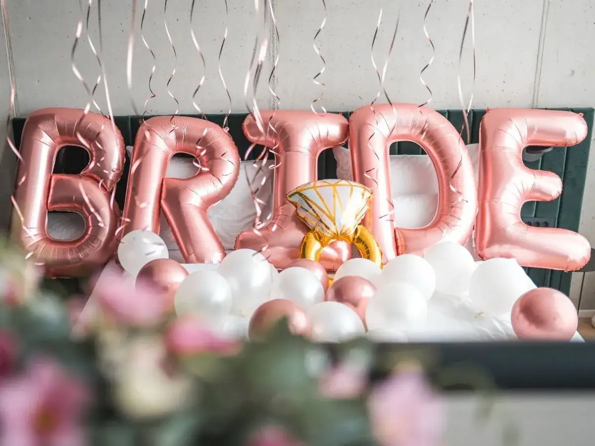 Różowe balony z napisem "BRIDE" i balon w kształcie pierścionka na łóżku. Idealne na wierszyki na panieński!