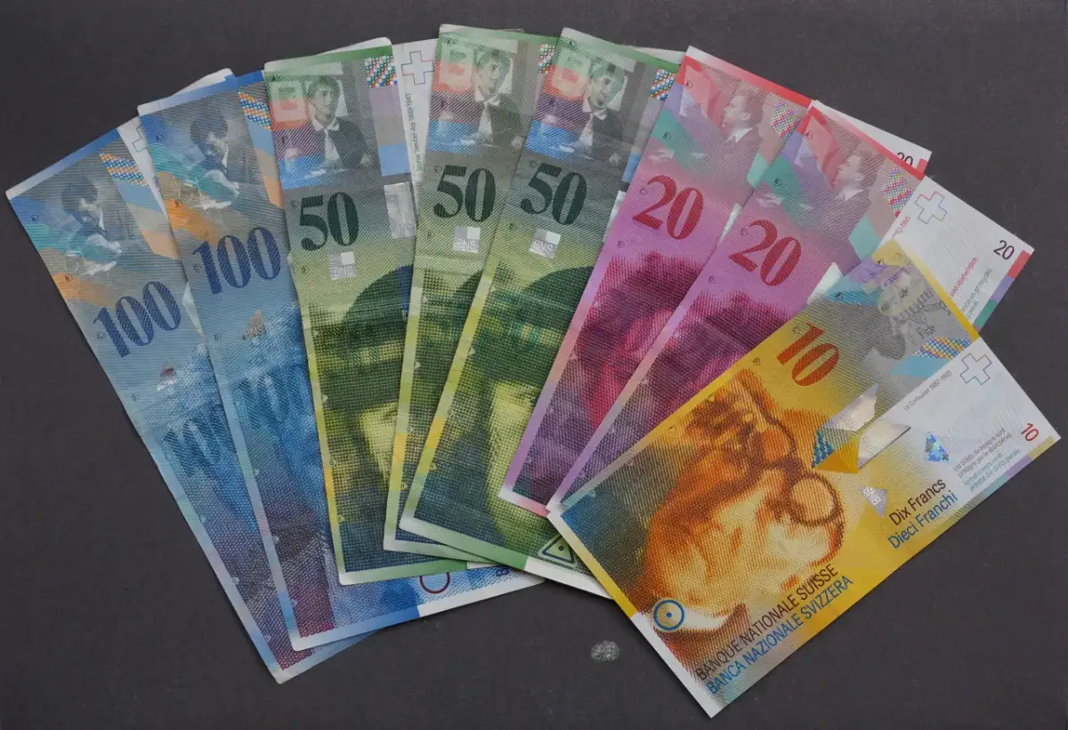 Różne banknoty CHF, czyli franków szwajcarskich, leżą na ciemnym tle. Widać nominały 10, 20, 50 i 100.