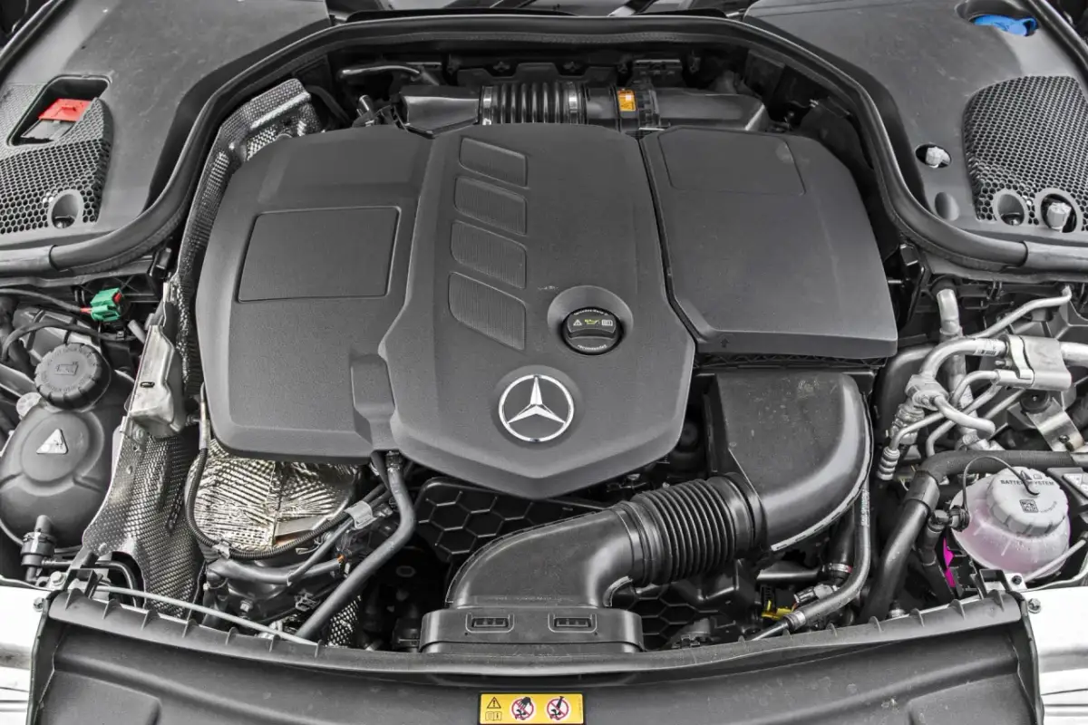 Silnik Mercedes-Benz E-Class. Widoczny czarny plastikowy dyfuzor, logo gwiazdy Mercedesa i elementy układu dolotowego.