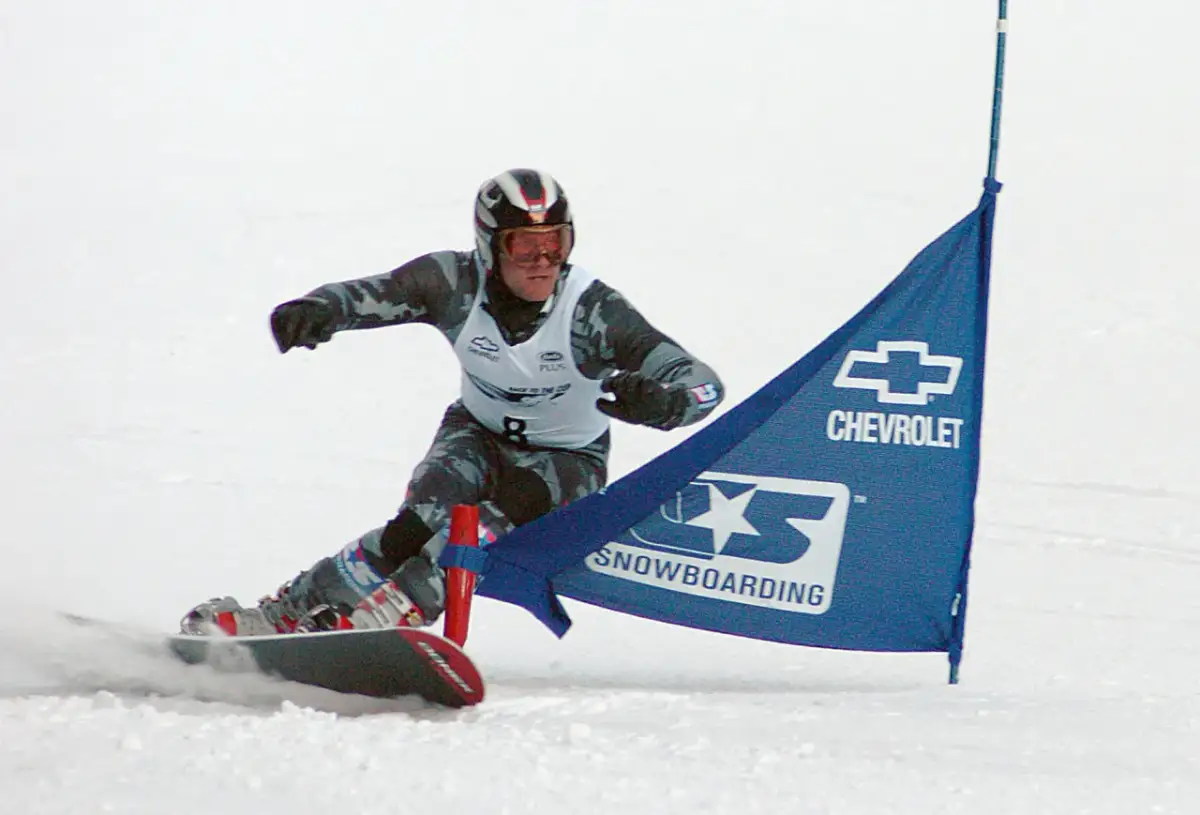 Snowboardzista w kasku i goglach mija niebieską flagę z logo Chevrolet. To sport, który zyskał popularność w XX wieku, choć jego korzenie sięgają wcześniejszych lat.