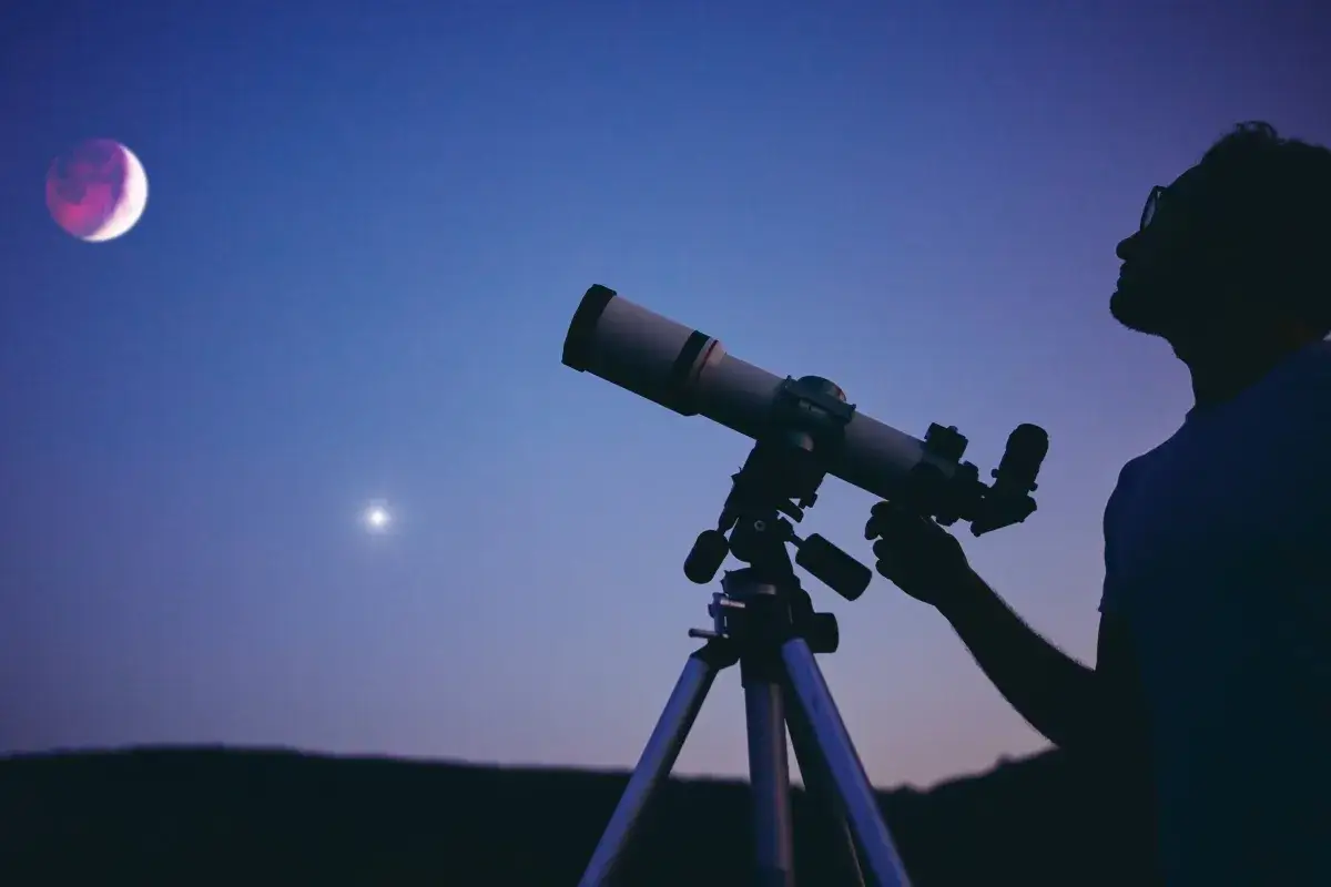 Sylwetka mężczyzny obserwującego przez teleskop księżyc i gwiazdę na nocnym niebie.