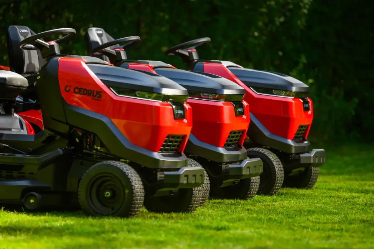 Trzy czerwono-czarne kosiarki do traktorka Cedrus stoją na zielonej trawie.