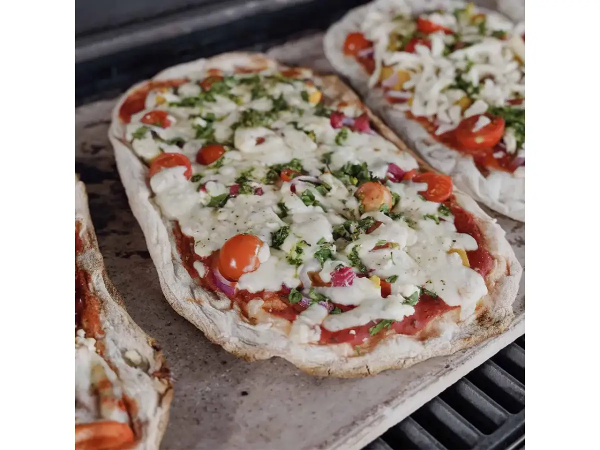 Dwie pizze na kamieniu, z pomidorkami i serem. Dowiedz się, jak przełożyć pizzę na kamień bez łopatki, by uzyskać idealnie chrupiący spód.