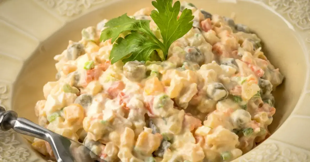 Sałatka jarzynowa w kremowym sosie, z groszkiem i marchewką, ozdobiona natką pietruszki. Zastanawiasz się, ile może stać sałatka jarzynowa w lodówce?