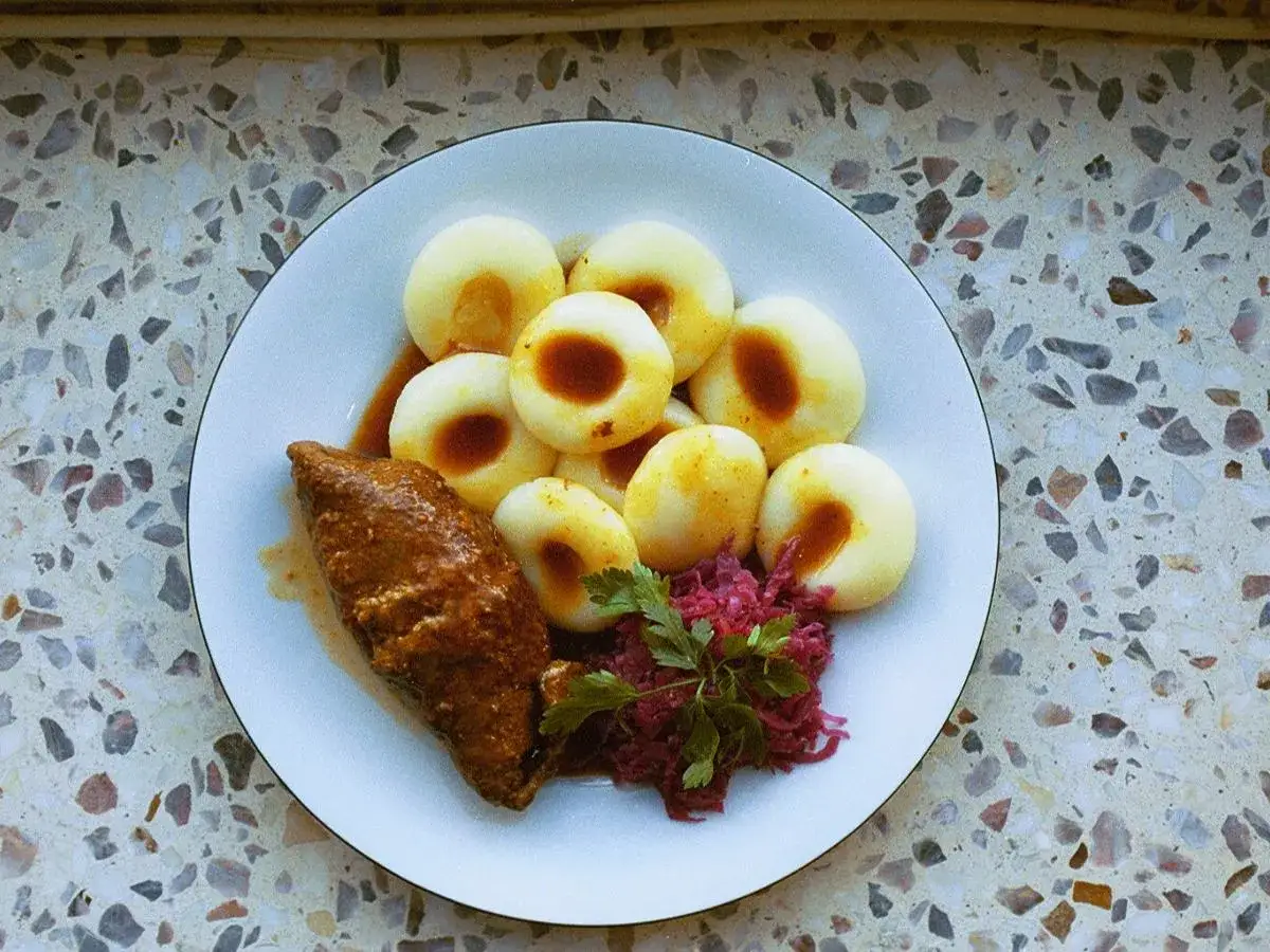 Jak gotować zamrożone kluski śląskie? Na talerzu kluski śląskie z sosem, roladą i czerwoną kapustą.